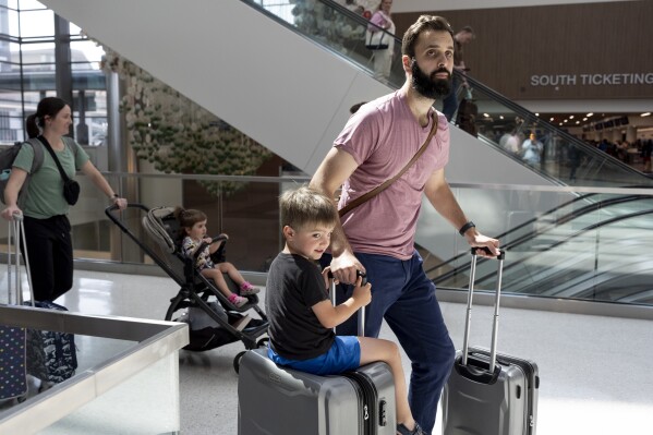 George Ridley, 4, kiri, mengendarai koper saat dia dan ayahnya, Chris Ridley, melewati Bandara Internasional Nashville, Kamis, 23 Mei 2024, di Nashville, Tennessee.  Jumlah orang Amerika diperkirakan akan melakukan perjalanan selama Akhir Pekan Hari Peringatan 2024. (AP Photo/George Walker IV)