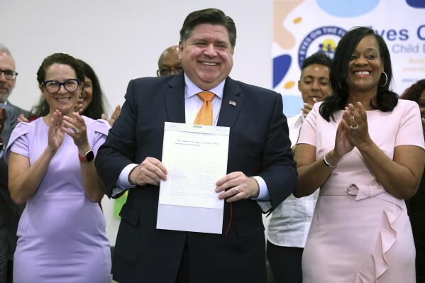  Illinois Gov. J.B. Pritzker holds up a newly signed bill at Eyes On The Future Child Development Center in Chicago, Tuesday, June 25, 2024, establishing the Illinois Department of Early Childhood. Illinois state Rep. Mary Beth Canty, left and state Sen. Kimberly A. Lightford, join him. (Terrence Antonio James/Chicago Tribune via AP)