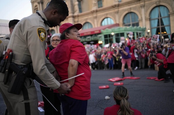 A Las Vegas police officer arrests a member of the Culinary Workers Union along the Strip, Wednesday, Oct. 25, 2023, in Las Vegas. Thousands of hotel workers fighting for new union contracts rallied Wednesday night on the Las Vegas Strip, where rush-hour traffic was disrupted when some members blocked the road before being detained by police. (AP Photo/John Locher)