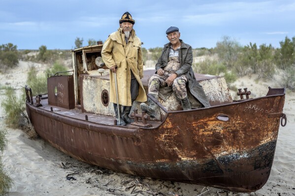 Ali Shadilov, left, and Anvar Saimbetov pose in front of an old boat in the area where the Aral Sea once was in Muynak, Uzbekistan, Tuesday, June 27, 2023.  interviewed Shadilov and others in Muynak, Uzbekistan – all residents in their 60s and 70s who’ve long been tied to the sea, or what remains of it. (AP Photo/Ebrahim Noroozi)