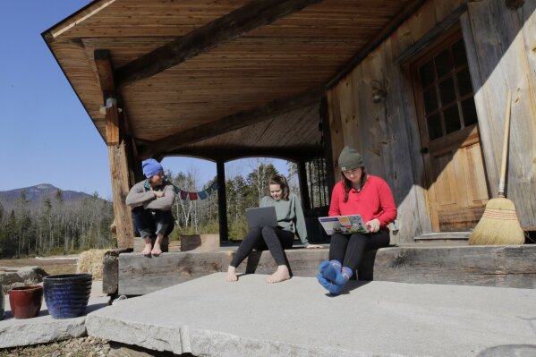 Ashley Bullard, left, sits on the porch of her family's rural home in North Sandwich, N.H., as her daughters Raven, center, a senior in high school, and Willow, right, a freshman at Brandeis University, try to complete their classwork from home during the virus outbreak on a very limited internet connection, Thursday, March 26, 2020. In the town of 1,200 best known as the setting for the movie “On Golden Pond," broadband is scarce. Forget streaming Netflix, much less working or studying from home. Even the police department has trouble uploading its reports.    (AP Photo/Charles Krupa)