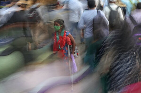 A woman wearing a face mask asks for alms as people rush to catch the train outside the Chhatrapati Shivaji Maharaj train terminus in Mumbai, India, Monday, Nov. 9, 2020. The global death toll from COVID-19 has topped 2 million. The milestone was reached just over a year after the coronavirus was first detected in the Chinese city of Wuhan. It is about equal to the population of Brussels, Mecca, Minsk or Vienna. It took eight months to hit 1 million lives lost. It took less than four months after that to reach the next million. (AP Photo/Rafiq Maqbool)