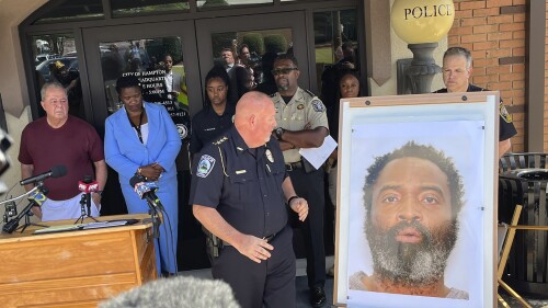 In this photo tweeted by WSB-TV's Steve Gehlbach, Hampton Police Chief James Turner, center, stands next to a mounted picture of suspect Andre Longmore during a news conference in Hampton, Ga., Saturday, July 15, 2023. Authorities are searching for Longmore, who is suspected of gunning down three men and a woman in Hampton. (Steve Gehlbach/WSB-TV via AP)