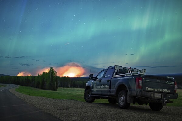 This photo provided by the Ministry of Water, Land and Resource Stewardship shows a wildfire, Aurora Borealis overhead, near Fort Nelson, British Columbia Saturday, May 11, 2024. An intense wildfire could hit a town in western Canada on Monday, based on forecasts of strong winds that have been fueling the out-of-control blaze which has already forced the evacuation of thousands, fire experts and officials warned. (Ministry of Water, Land and Resource Stewardship/The Canadian Press via AP)