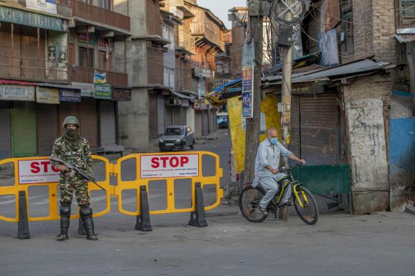 A Kashmiri cycles past a barricade set up as road blockade as a paramilitary soldier stands guard on the first anniversary of India’s decision to revoke the disputed region’s semi-autonomy, in Srinagar, Indian controlled Kashmir, Wednesday, Aug. 5, 2020. Last year on Aug. 5, India’s Hindu-nationalist-led government of Prime Minister Narendra Modi stripped Jammu-Kashmir of its statehood and divided it into two federally governed territories. Late Tuesday, authorities lifted a curfew in Srinagar but said restrictions on public movement, transport and commercial activities would continue because of the coronavirus pandemic. (AP Photo/ Dar Yasin)
