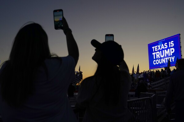 FILE - People hold their cellphones as they wait for the plane carrying former President Donald Trump to take off after a campaign rally at Waco Regional Airport Saturday, March 25, 2023, in Waco, Texas. (AP Photo/Nathan Howard, File)