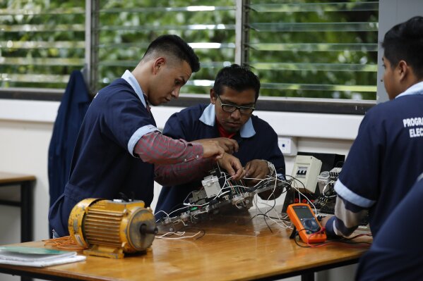 In this Oct. 11, 2019, photo, José Fernando Guillén Rodríguez, 21, left, practices building circuits with other students around a workbench in San Salvador, El Salvador. "I don't think about migrating anymore," said Guillén Rodríguez, 21, who was apprehended in the U.S. at 18 and spent time in adult detention before being deported. Now he's completed a year of daily electrical classes and works as an apprentice at an electrical construction company. (AP Photo/Eduardo Verdugo)