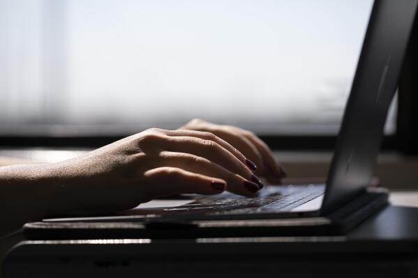 FILE - This May 18, 2021, photo shows a woman typing on a laptop on a train in New Jersey.  With fewer employees working in offices, several companies have begun turning toward off-site retreats and meetups to foster connection and improve employee morale. These off-site experiences are flipping traditional business travel on its head: Rather than emphasizing coworking, meetings and other work-centric itineraries, off-site retreats are often designed to encourage relationship building.  (AP Photo/Jenny Kane, File)