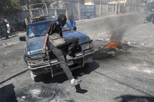 A protester sits on the hood of a car during a demonstration to demand government action against gang violence in Port-au-Prince, Haiti, Thursday, Feb. 20, 2025. (AP Photo/Odelyn Joseph)