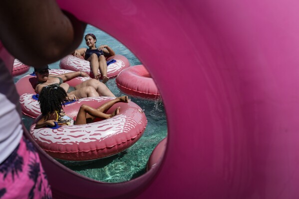 Visitantes flotan en tubos inflables rosas en el parque acuático Parque Dunas en Valencia, Venezuela, el domingo 28 de enero de 2024. (Foto AP/Mathias Delacroix)
