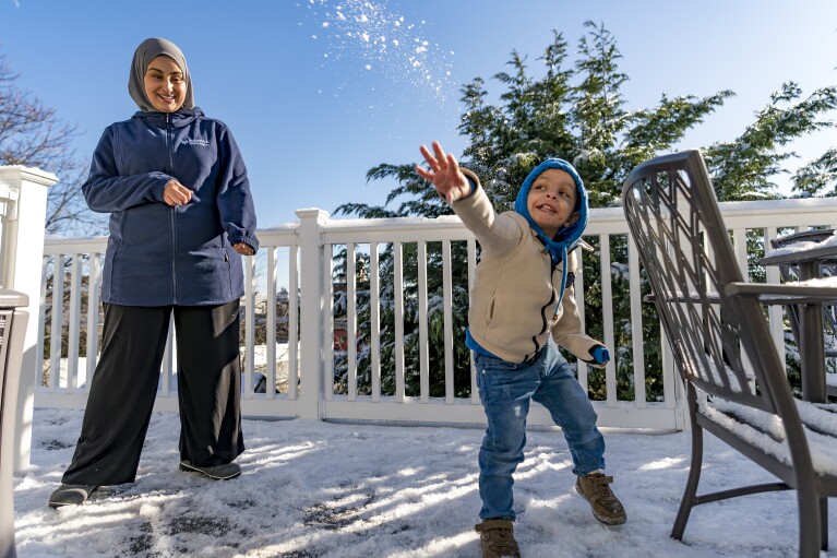 Omar Abu Kuwaik, throws snow shortly after arriving from Gaza at the residence of the Global Medical Relief Fund as Khaolah Obahi of Rahma Worldwide looks on, Wednesday, Jan. 17, 2024, in the Staten Island borough of New York. The snow was the first that the 4-year-old had ever experienced. (AP Photo/Peter K. Afriyie)