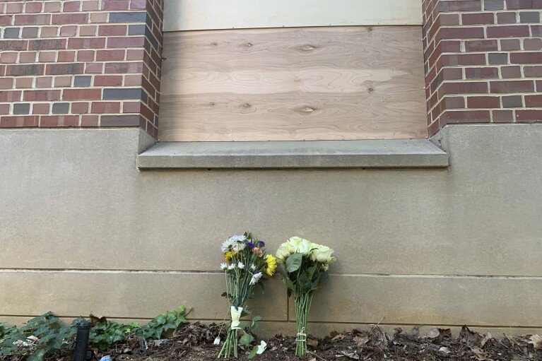 Flowers lay under a boarded up window at Caudill Labs on the UNC-Chapel Hill campus in Chapel Hill, N.C., Tuesday, Aug. 29, 2023, after a graduate student fatally shot his faculty adviser. A bullet hole could be seen earlier Tuesday in the bottom left corner of that window. (AP Photo/Hannah Schoenbaum)