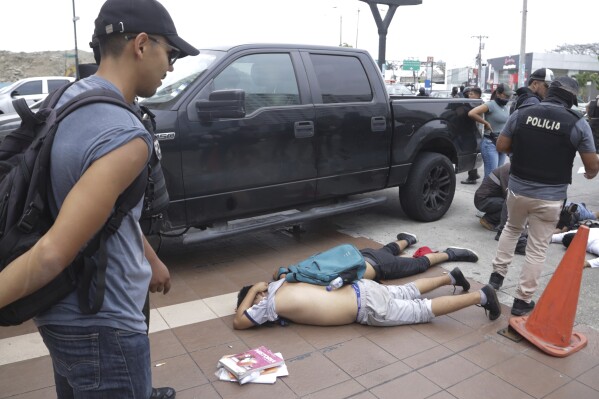 Men lie face down on the ground, detained by police outside TC Television, after a producer told police that they were part of a group who broke onto their set during a live broadcast, although they had not entered the station, in Guayaquil, Ecuador, Tuesday, Jan. 9, 2024. The country has seen a series of attacks after the government imposed a state of emergency in the wake of the apparent escape of a powerful gang leader from prison. (AP Photo/Cesar Munoz)