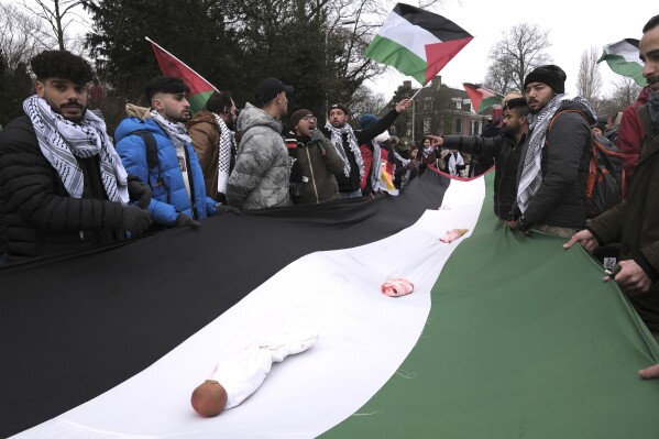Protestors carry a giant Palestinian flag, with dolls wrapped to represent dead and injured children, during a demonstration outside the International Court of Justice in The Hague, Netherlands, Thursday, Jan. 11, 2024. The United Nations' top court opens hearings Thursday into South Africa's allegation that Israel's war with Hamas amounts to genocide against Palestinians, a claim that Israel strongly denies. (AP Photo/Patrick Post)