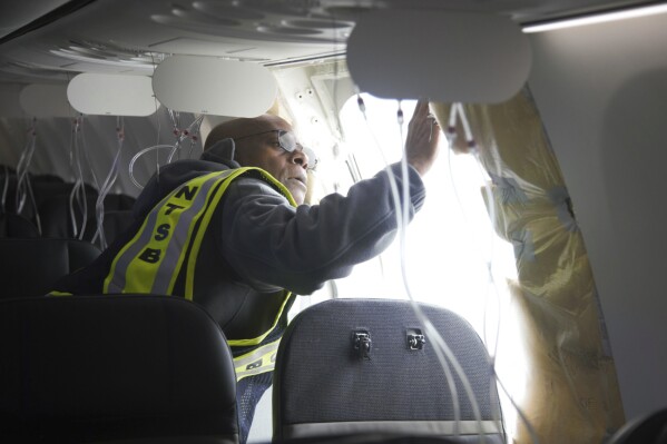 In this photo released by the National Transportation Safety Board, NTSB Investigator-in-Charge John Lovell examines the fuselage plug area of Alaska Airlines Flight 1282 on Sunday, Jan. 7, 2024, in Portland, Ore. A panel used to plug an area reserved for an exit door on the Boeing 737 Max 9 jetliner blew out Friday night shortly after the flight took off from Portland, forcing the plane to return to Portland International Airport. (National Transportation Safety Board via AP)