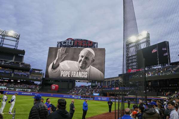 Fans and players stand during a moment of silence as a portrait of Pope Francis is displayed at Citi Field before a baseball game between the New York Mets and the Philadelphia Phillies Monday, April 21, 2025, in New York. (AP Photo/Frank Franklin II)