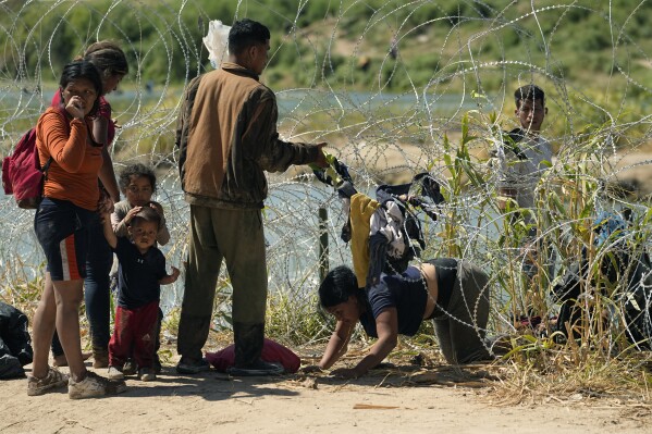 Migrantes que cruzaron a Estados Unidos desde México pasan por debajo de un alambre con cuchillas en al frontera del Río Bravo, el 21 de septiembre de 2023, en Eagle Pass, Texas. (AP Foto/Eric Gay)