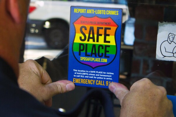 FILE - In this June 24, 2015 photo, Officer Jim Ritter places a "Safe Place" sticker on the window of a business in Seattle's Capitol Hill neighborhood. Some central Florida lawmakers said they are considering “all legislative, legal and executive options available” to stop business owners in a small town from voluntarily displaying rainbow decals in their windows indicating that they are “safe places” for LGBTQ people who feel threatened.(Ellen M. Banne/The Seattle Times via AP, File)