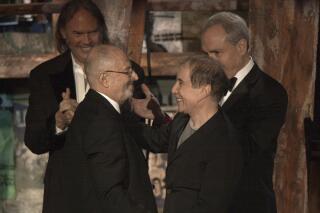 FILE - Record executive Mo Ostin, foreground left, is embraced by singer/songwriter Paul Simon, right, as singer/songwriter Neil Young, background left, and producer Lorne Michaels look on after Ostin was inducted into the Rock and Roll Hall of Fame in New York on March 10, 2003. Ostin, a self-effacing giant of the music business who with rare integrity presided over Warner Bros. Records’ rise to a sprawling, billion-dollar empire, died Sunday, July 31, 2022. He was 95. (AP Photo/Gregory Bull, File)