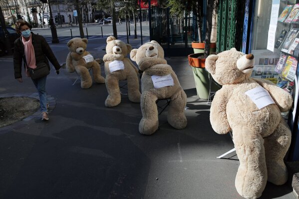 A woman wearing a protective mask walks by a shop with bears installed in line to show social distancing in Paris, Tuesday, March 24, 2020. French President Emmanuel Macron urged employees to keep working in supermarkets, production sites and other businesses that need to keep running amid stringent restrictions of movement due to the rapid spreading of the new coronavirus in the country. For most people, the new coronavirus causes only mild or moderate symptoms. For some it can cause more severe illness, especially in older adults and people with existing health problems. (AP Photo/Francois Mori)