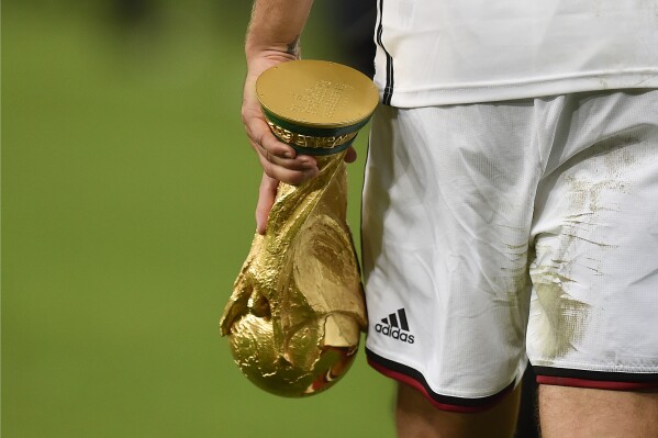 FILE - Germany's national player Lukas Podolski leaves the pitch with the World Cup trophy in his hand, wearing Adidas after winning the World Cup final soccer match in Rio de Janeiro, Brazil, Sunday, July 13, 2014. The German Football Association DFB announced today, that Nike will replace Adidas as the new supplier of the national teams from 2027. (AP Photo/Martin Meissner, File)