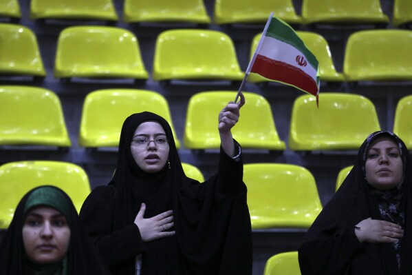 Iranian women listen to their country's national anthem as one of them waves the national flag during an election campaign rally ahead of the March 1, parliamentary and Assembly of Experts elections, in Tehran, Iran, Tuesday, Feb. 27, 2024. Iran is holding parliamentary elections this Friday, yet the real question may not be who gets elected but how many people actually turn out to vote. Separately, Iranians will also vote on Friday for members of the country's 88-seat Assembly of Experts, an eight-year term on a panel that will appoint the country's next supreme leader after Khamenei, 84. (AP Photo/Vahid Salemi)