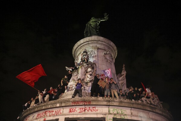 People climb on the statue at Republique plaza during a protest against the far-right National Rally party which came out strongly ahead in first-round legislative elections, Sunday, June 30, 2024 in Paris. (AP Photo/Thomas Padilla)