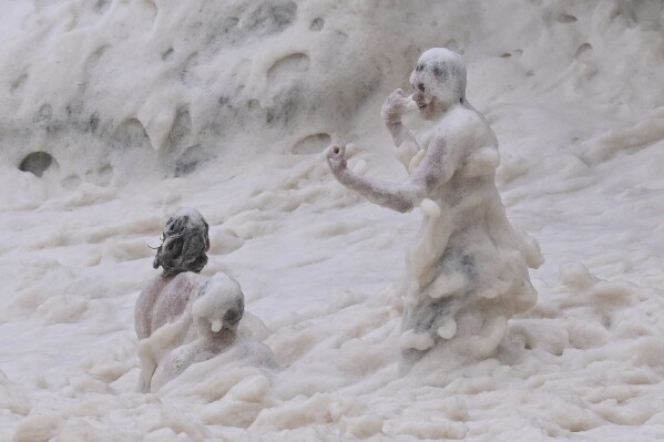 Children play in sea foam in the Coolangatta area of Gold Coast, Australia, Friday, March 7, 2025. (Dave Hunt/AAP Image via AP)