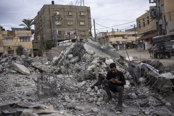 Ibrahim Hasouna, center, the sole survivor among his family, sits amidst the debris of his bombed home in Rafah, southern Gaza Strip, Tuesday, Feb. 13, 2024. On Monday, February 12, Hasouna lost eight family members, including three children, He says the house was bombed during an Israeli operation to rescue hostages held in a building in another part of town. (AP Photo/Fatima Shbair)