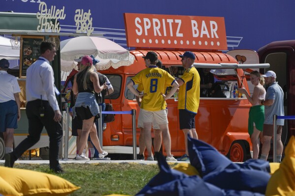 Spectators gather near food trucks at the Marco Simone Golf Club in Guidonia Montecelio, Italy, Wednesday, Sept. 27, 2023. The Ryder Cup's food scene is decidedly local at the Marco Simone club outside Rome. There's an "APECESARE" food truck named after Julius Caesar selling "Street Food Romano" where the menu highlight is a carbonara burger with Damini beef, carbonara sauce, guanciale, Soncino lettuce, pepper and caramelized onion. Vendor Alessandro Favola says "eat one and you're all set." Another option at the same truck is a cacio e pepe burger based on another classic Roman pasta. Both burgers sell for 23 euros ($24) with fries. (AP Photo/Gregorio Borgia)