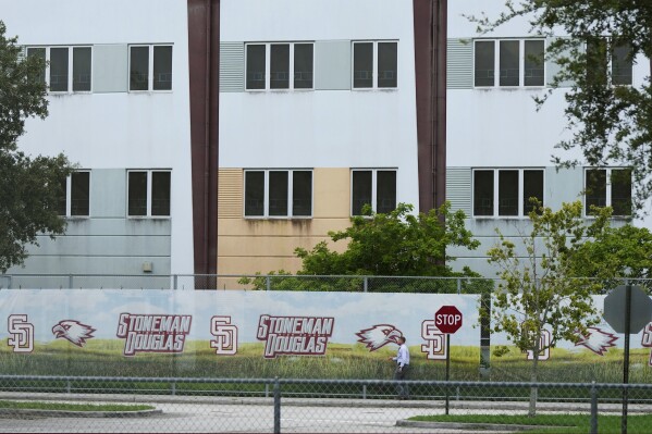 FILE - A security agent walks alongside a barrier surrounding Marjory Stoneman Douglas High School, July 5, 2023, in Parkland, Fla. Demolition of the building where 17 people died in the 2018 Parkland school shooting is set to begin, as crews will begin tearing down the three-story building at the high school on Thursday, June 13, 2024. (AP Photo/Rebecca Blackwell, File)