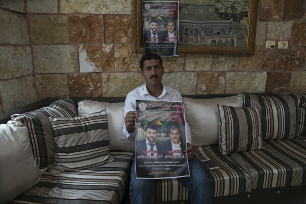 Abdelazim Wadi, 50, holds up a poster commemorating his brother, Ibrahim Wadi, and his nephew, Ahmed Wadi, who were killed by Israeli settlers during a funeral procession on Oct. 12 in the rural Palestinian village of Qusra, West Bank, Sunday, Nov. 12, 2023. With the world’s attention focused on the fighting in Gaza, Israeli settler violence against Palestinians since Oct. 7 has surged to the highest levels ever recorded by the United Nations. Palestinians say this Israel-Hamas war has left them more scared and vulnerable than ever in recent memory. (AP Photo/Mahmoud Illean)