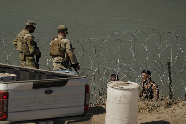 Guardsmen talk with migrants trying to cross the Rio Grande from Mexico into the U.S. near in Eagle Pass, Texas, Tuesday, July 11, 2023. Texas Republican Gov. Greg Abbott has escalated measures to keep migrants from entering the U.S. He's pushing legal boundaries along the border with Mexico to install razor wire, deploy massive buoys on the Rio Grande and bulldozing border islands in the river. (AP Photo/Eric Gay)