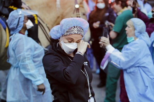 FILE - A medical worker reacts as police officers and pedestrians cheer medical workers outside NYU Medical Center in New York, April 16, 2020. Some states that stockpiled millions of masks and other personal protective equipment during the coronavirus pandemic are now throwing the items away. (AP Photo/Frank Franklin II, File)