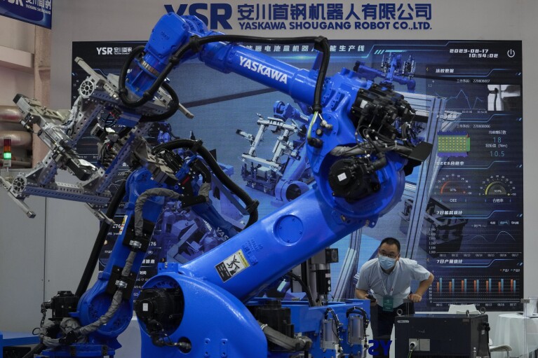 A man looks at the industrial robotic arms from Yaskawa Shougang Robot Co. Ltd on display at the annual World Robot Conference at the Etrong International Exhibition and Convention Center on the outskirts of Beijing, Thursday, Aug. 17, 2023. (AP Photo/Andy Wong)