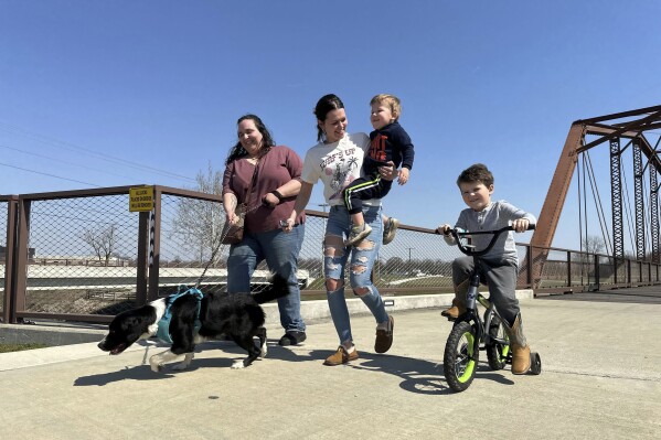 From left; Emerson Howard and dog Dixie enjoy a walk along with Destiny Porter and her children, 2-year old Merrick Mercer and 4-year old Maxton Mercer at the Kitselman bridge connecting the Cardinal and White River Greenway trails in Muncie, Ind., Wednesday, March 13, 2024. The Cardinal Greenways pathway born from eastern Indiana's abandoned railroad tracks will become a central cog in the Great American Rail Trail — a planned 3,700-mile network of uninterrupted trails spanning from Washington state to Washington, D.C. (AP Photo/Isabella Volmert)