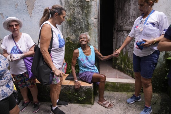 Zuleida greets and speaks with municipal health workers and volunteers who are inspecting the Tabajaras favela for standing water where Aedes aegypti mosquitoes can breed, in an effort to stop the spread of dengue in the Copacabana neighborhood of Rio de Janeiro, Brazil, Wednesday, Feb. 7, 2024. (AP Photo/Silvia Izquierdo)