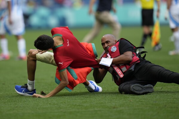 A steward catches a pitch invader during the men's Group B soccer match between Argentina and Morocco at Geoffroy-Guichard Stadium at the 2024 Summer Olympics, Wednesday, July 24, 2024, in Saint-Etienne, France. (ĢӰԺ Photo/Silvia Izquierdo)