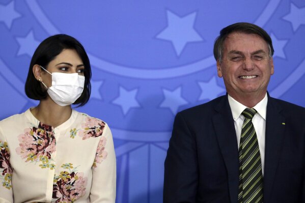 Brazil's President Jair Bolsonaro smiles sitting next to his wife Michelle Bolsonaro wearing a protective face mask, during the swearing ceremony of his new justice minister, at the Planalto presidential palace, in Brasilia, Brazil, Wednesday, April 29, 2020. (AP Photo/Eraldo Peres)