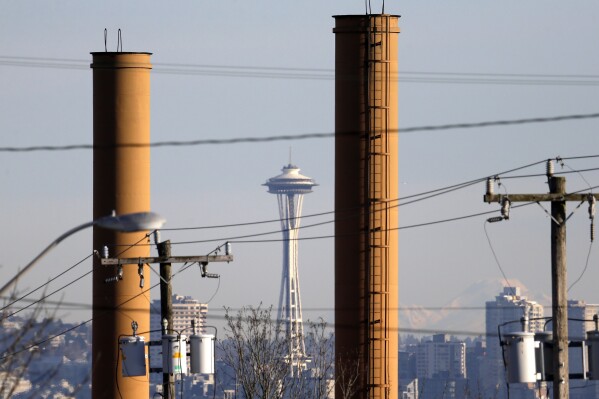 FILE - The Space Needle is seen in view of still-standing but now defunct stacks at a steel plant in Seattle on Feb. 25, 2016. A conservative-backed effort to repeal Washington state's landmark carbon pricing program and tax on the sale of stocks and bonds is putting the budget into limbo, with billions of dollars at stake and just days left in this year's Legislative session. (AP Photo/Elaine Thompson, File)