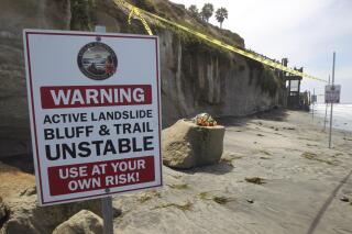 FILE - One of several warning signs is posted next to the sand rock debris left from a sea cliff collapse that killed three people near the Grandview Beach access stairway in the beach community of Leucadia in Encinitas, Calif., on Aug. 3, 2019. Officials say California will provide $300 million to help relocate train tracks along a stretch of eroding seaside cliffs near San Diego. The funding to relocate the tracks in Del Mar further inland comes as part of California's $308 billion state budget signed by Gov. Gavin Newsom last week. (Hayne Palmour IV/The San Diego Union-Tribune via AP, File)
