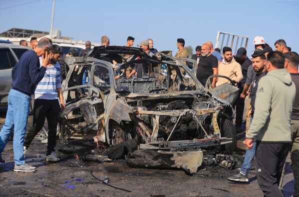 People gather near a charred car that was hit by an Israeli strike, in the southern coastal town of Ghazieh, Lebanon, Friday, April 18, 2025. (AP Photo/Mohammed Zaatari)