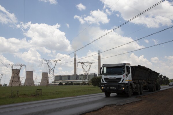 FILE — A coal truck, right, passes the coal-powered Duvha power station, near Emalahleni (formerly Witbank) east of Johannesburg, Thursday, Nov. 17, 2022. South African authorities say they have carried out search and seizure operations across five provinces to break up a huge coal-smuggling syndicate that cost the country more than $26 million and contributed to the breakdown of some of its state-owned power stations and an ongoing power crisis. (AP Photo/Denis Farrell/File)