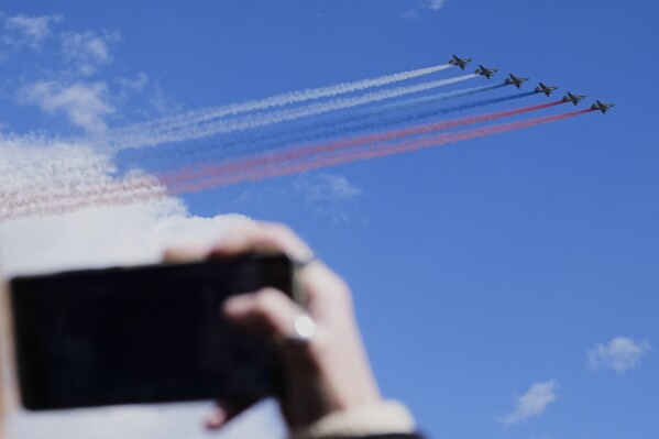 A woman takes pictures as Russian Air Force Su-25 jets fly over Red Square leaving trails of smoke in the colors of Russian state flag during the Victory Day military parade in Moscow, Russia, Friday, May 9, 2025, during celebrations of the 80th anniversary of the Soviet Union's victory over Nazi Germany during the World War II. (AP Photo/Pavel Bednyakov, Pool)