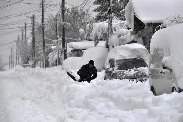 A man shovels snow, as he tries to clear his car in town of Isperih, Northeast Bulgaria, Sunday, Nov. 26, 2023. Bulgaria's government declared a state of emergency in large parts of the Balkan country after heavy snow and powerful winds caused power outages, closed roads, traffic accidents and travel delays. (AP Photo/Bulgarian News Agency)