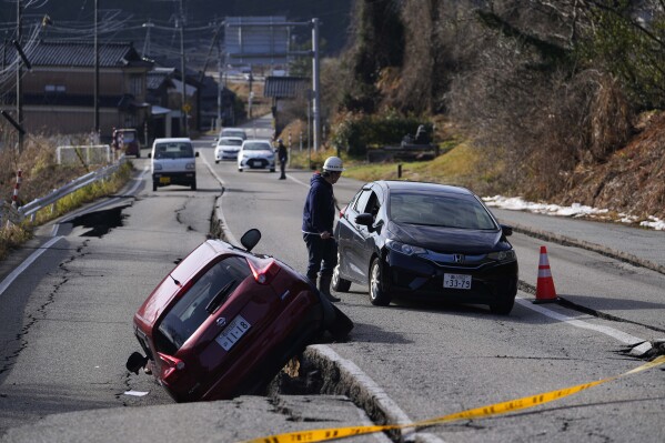 A man directs a driver moving through a damaged street near Anamizu town in the Noto peninsula facing the Sea of Japan, northwest of Tokyo, Tuesday, Jan. 2, 2024, following Monday's deadly earthquake. A series of powerful earthquakes that hit western Japan damaged thousands of buildings, vehicles and boats. Officials warned that more quakes could lie ahead. (AP Photo/Hiro Komae)
