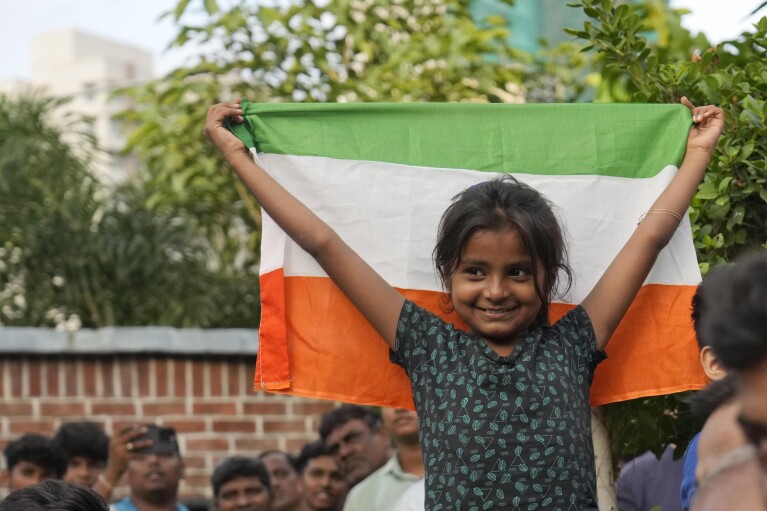 A girl stands with the Indian national flag as she watches a live telecast of the landing og Chandrayaan-3, or “moon craft” in Sanskrit, in Mumbai, India, Wednesday, Aug. 23, 2023. (AP Photo/Rajanish Kakade)
