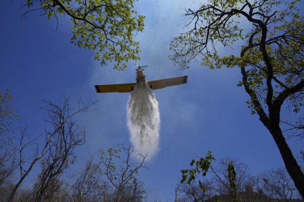 A plane drops water on a fire in the Serra do Coco forest area in Riachao das Neves, Bahia state, Brazil, Friday, Sept. 22, 2023. According to the National Center for Prevention and Combat of Forest Fires, the fires are being fanned by strong winds, high temperatures and dry weather. (AP Photo/Eraldo Peres)