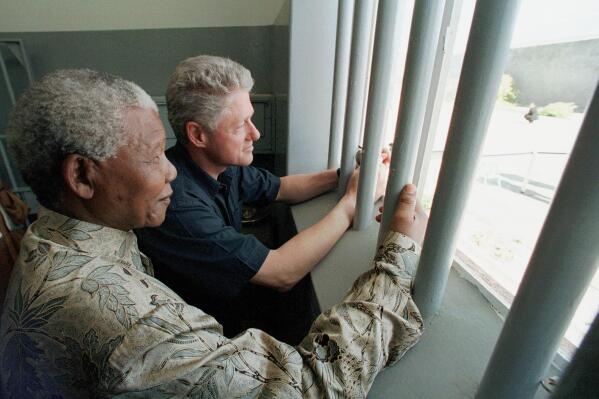 FILE - Nelson Mandela, left, and former US president Bill Clinton look to the outside from Mandela's Robben Island prison cell in Cape Town, South Africa, March 27, 1998. A South African Cabinet minister on Friday Dec. 24, 2021, urged the cancellation of an upcoming U.S. auction of a key to the Robben Island prison cell where Nelson Mandela, the country's first Black president, was long jailed for his opposition to apartheid. (AP Photo/Scott Applewhite, Pool, File)