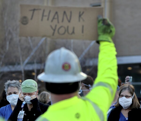 FILE - In this April 22, 2020, file photo healthcare workers, including ER nurse Tamra Hill, front left, wiping away tears, at Regions Hospital to thank Xcel Energy crew members, including Paul Peikert, who had lined the street outside Regions to greet healthcare workers at a morning shift change in St. Paul, Minn. Fewer than one-third of the states have enacted policies that shift the burden of proof for coverage of job-related COVID-19 so workers like first responders and nurses don't have to show they got sick by reporting for a risky assignment. (David Joles/Star Tribune via AP, File)